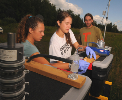 Undergraduate research students Lisa D'Auria (left) and Jessica Castilleja (center) unpack and set up bioaerosols sampling equipment under the direction of graduate student Michael Jahne (right).