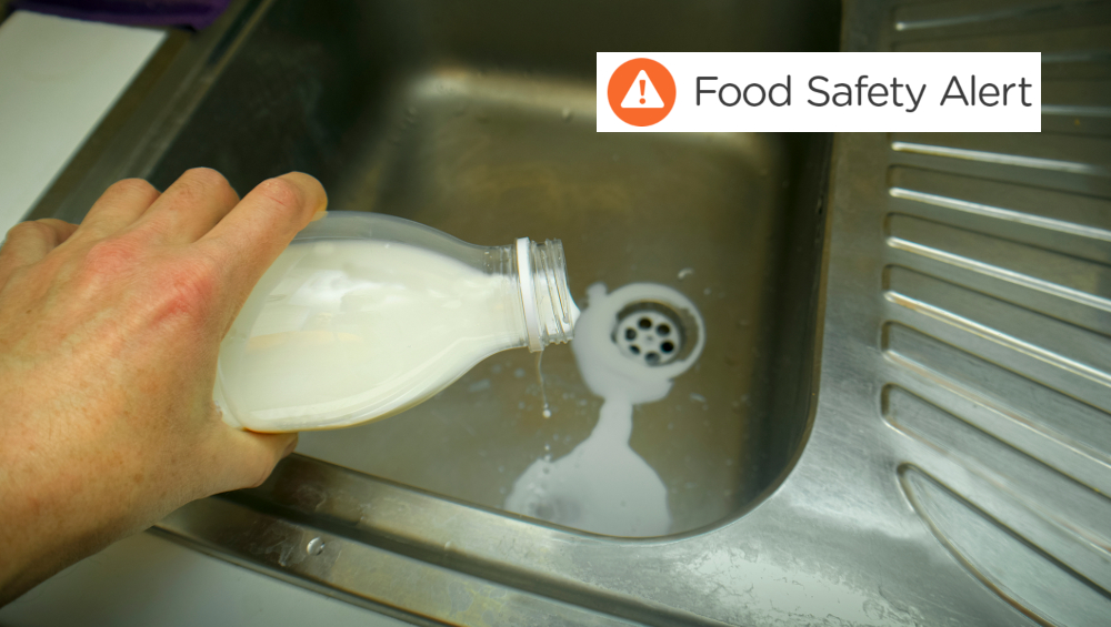 A hand with bottle of milk seems gone off over a kitchen sink