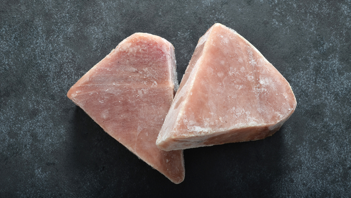 Two frozen tuna fish steaks on dark backgound shot from above