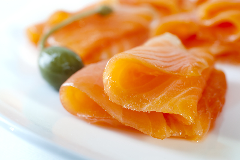 Cold smoked salmon on a white plate with a caperberry