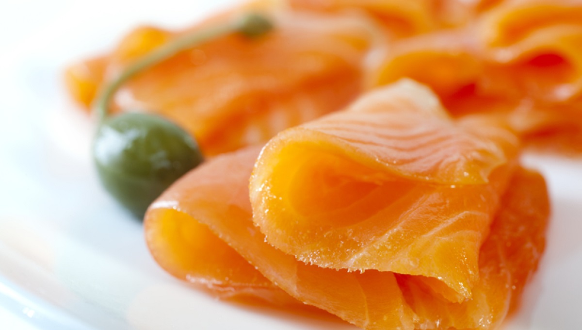 Cold smoked salmon on a white plate with a caperberry